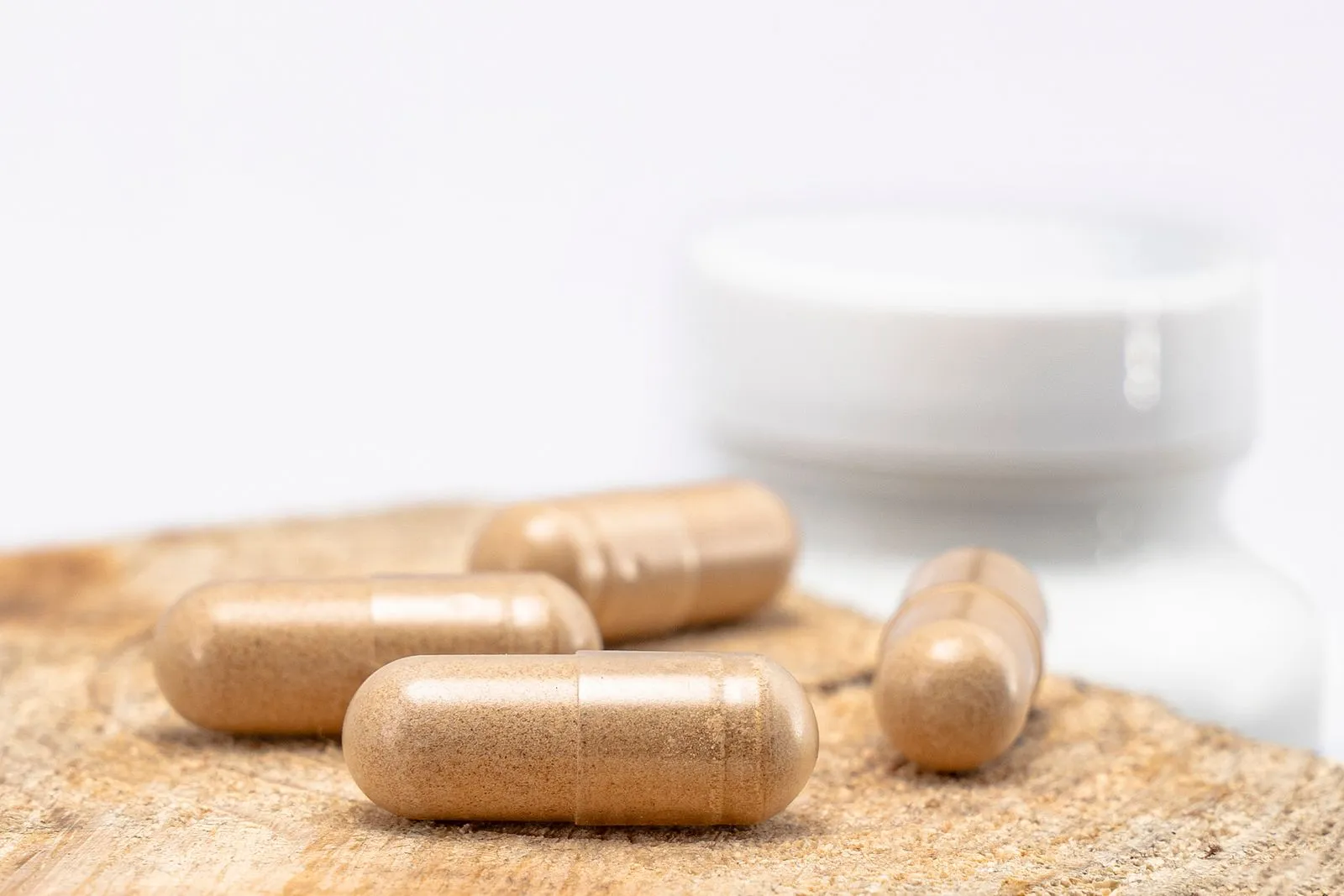 Brown supplement capsules resting on a wooden surface beside a blurred bottle