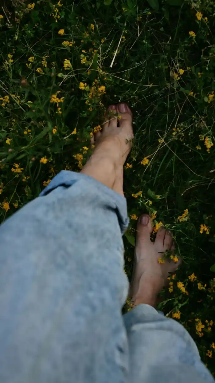Bare feet walking through grass and yellow wildflowers