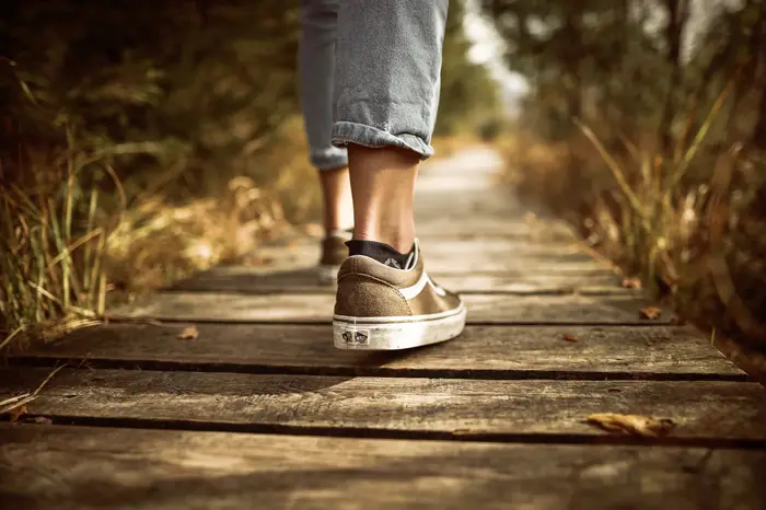 A person walking in supportive sneakers along a sunlit wooden boardwalk path