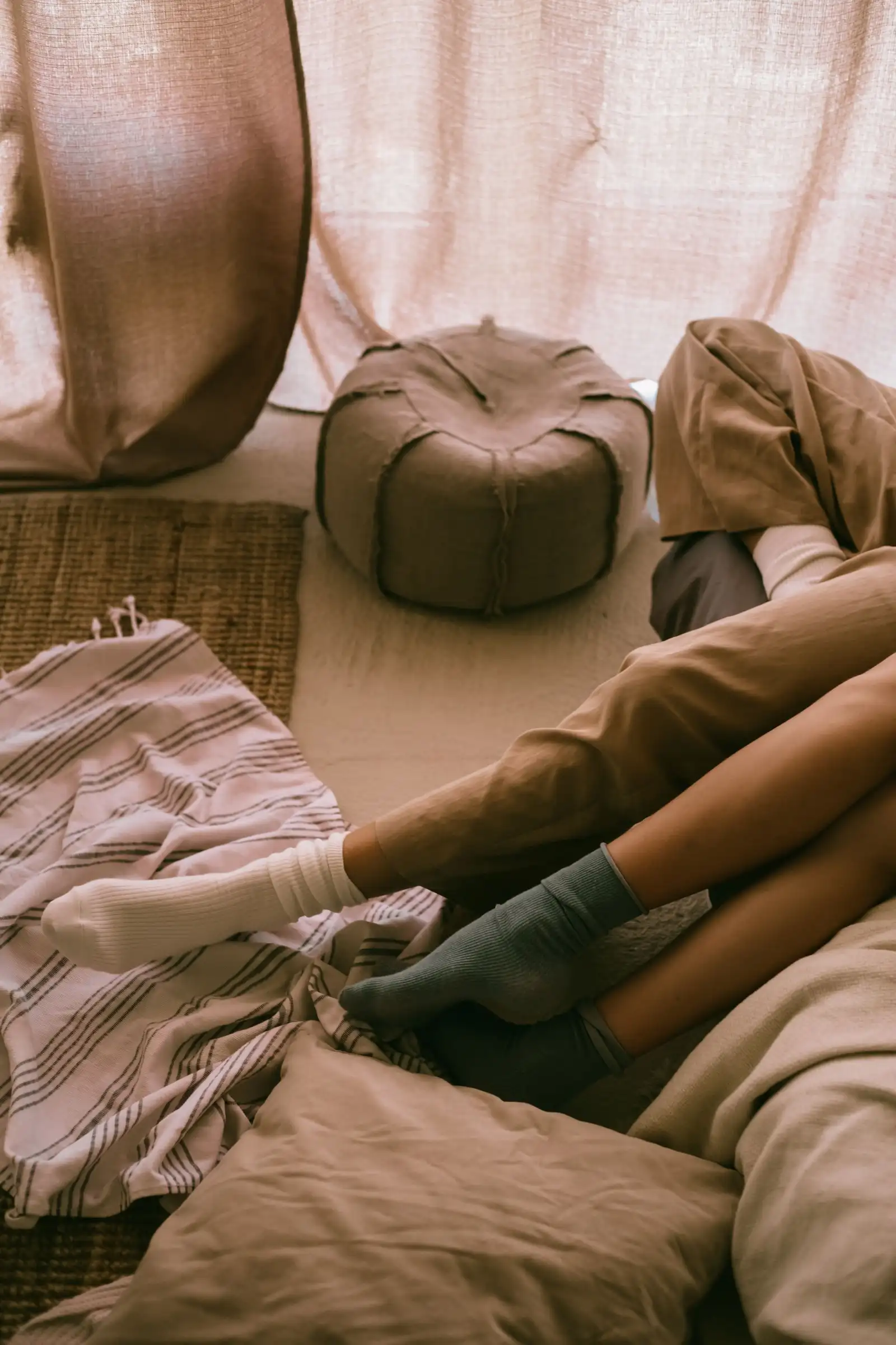 Two feet in cozy socks tucked into warm blankets in soft, muted light