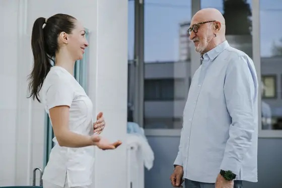 A smiling doctor talking with an older patient in a bright, calm clinic hallway