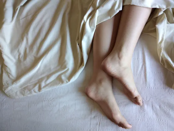 Bare feet and ankles crossed, resting on soft cream-colored bedding