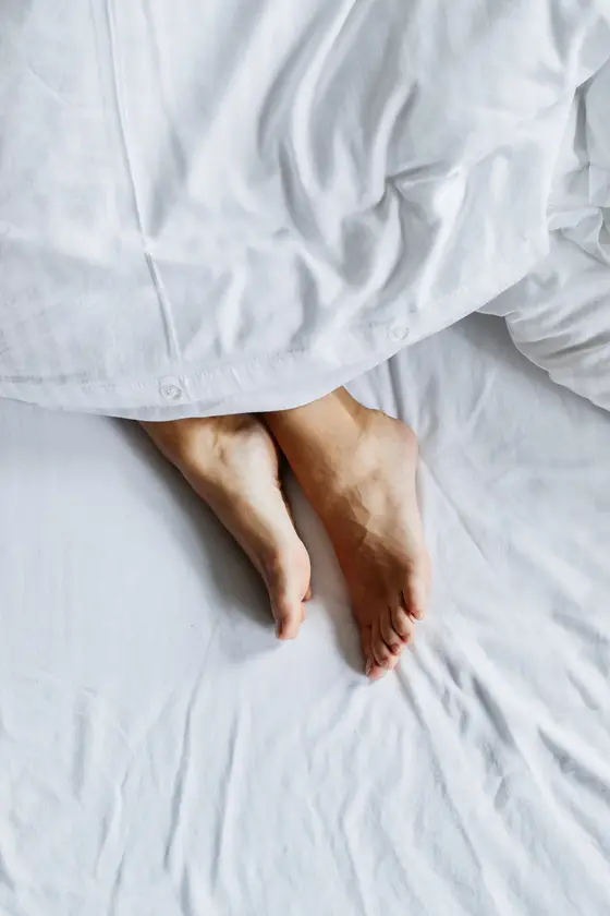 Bare feet resting outside white bed covers at night