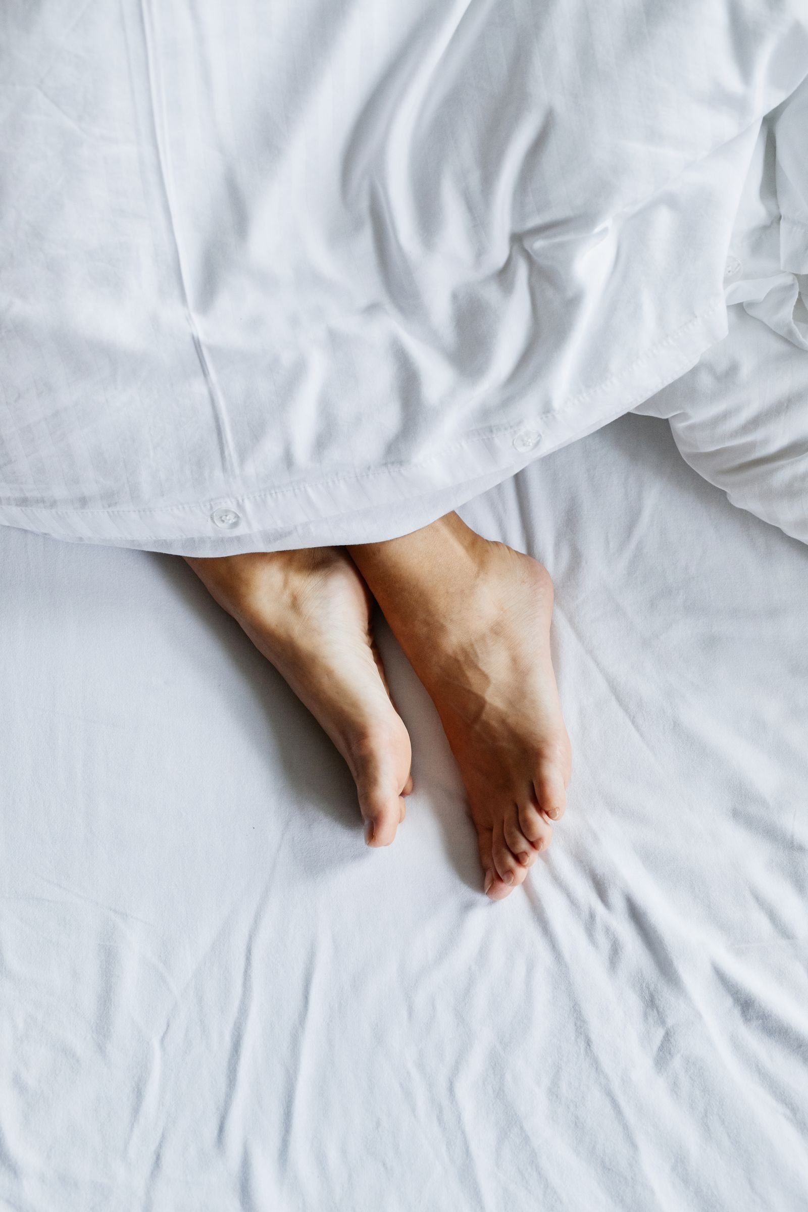 Bare feet resting outside white bed covers at night