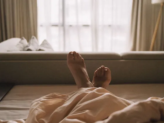Bare feet peeking out from under a warm cream-colored blanket in soft morning light