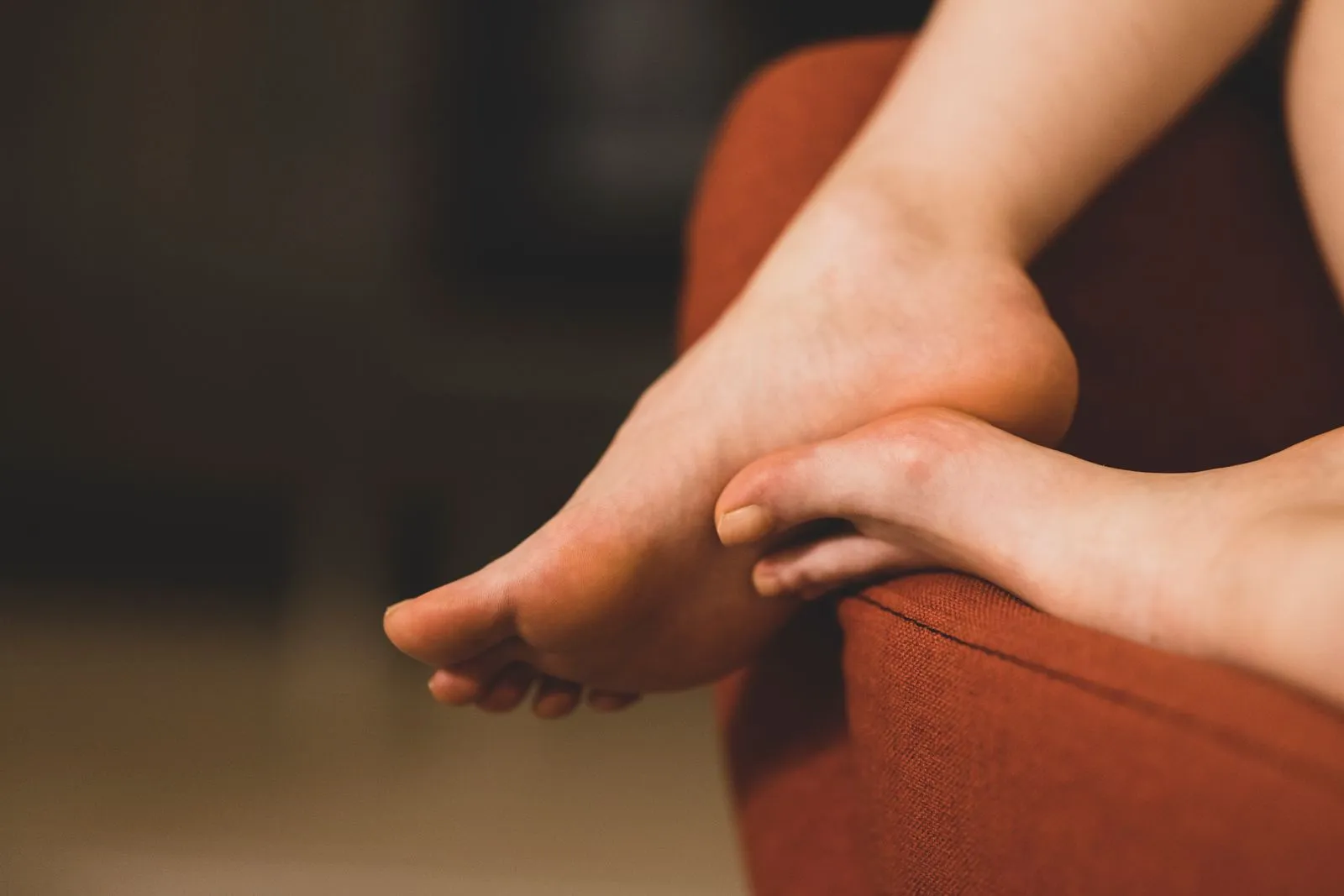 Bare feet resting on the arm of a warm terracotta-colored armchair in soft evening light