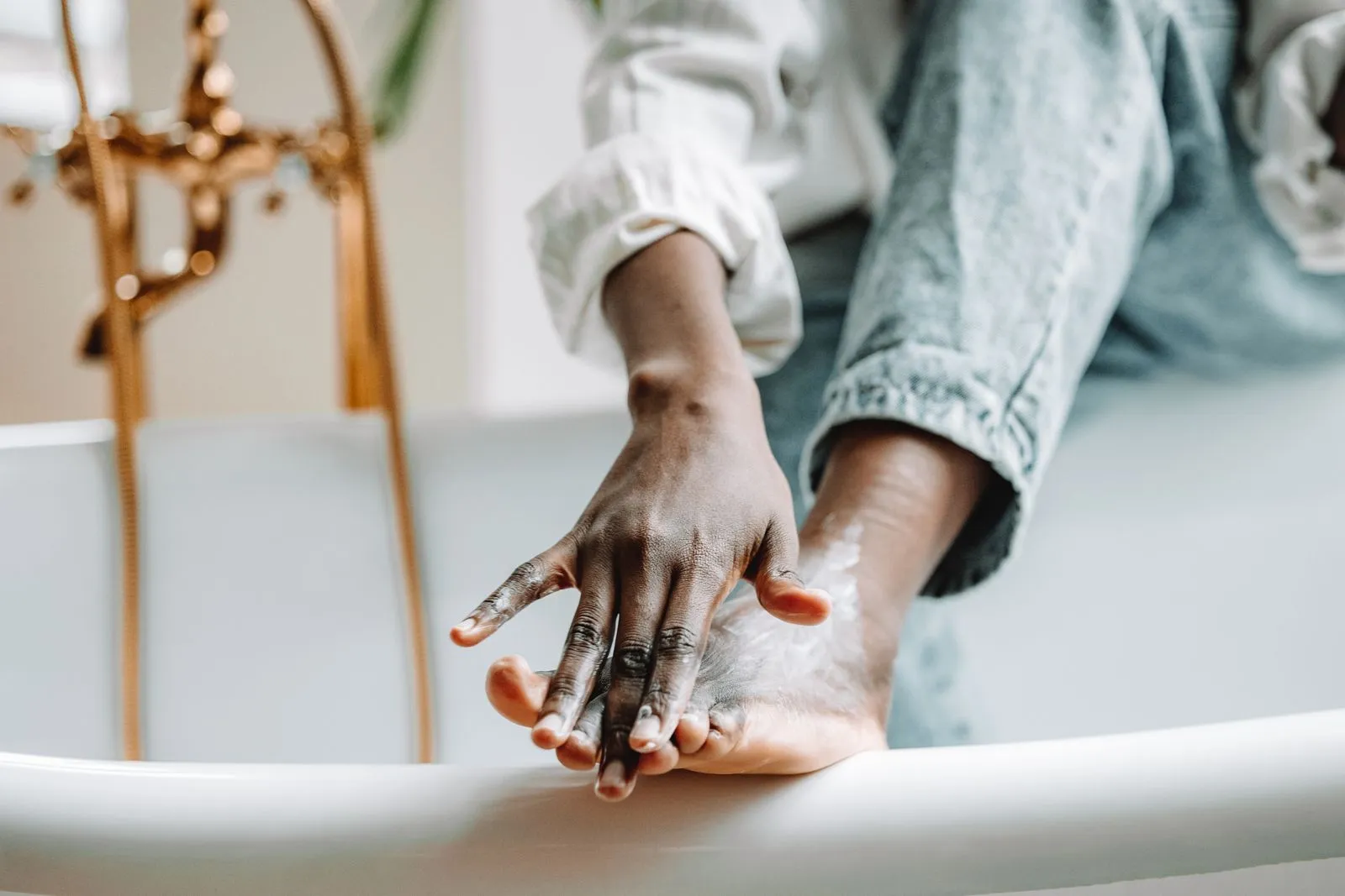 A hand applying cream to a foot resting on the edge of a bathtub