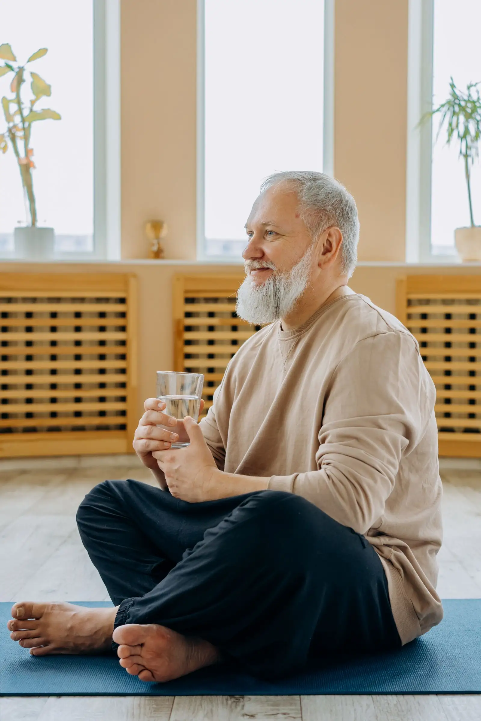 An older man sitting cross-legged in warm morning light, holding a glass of water