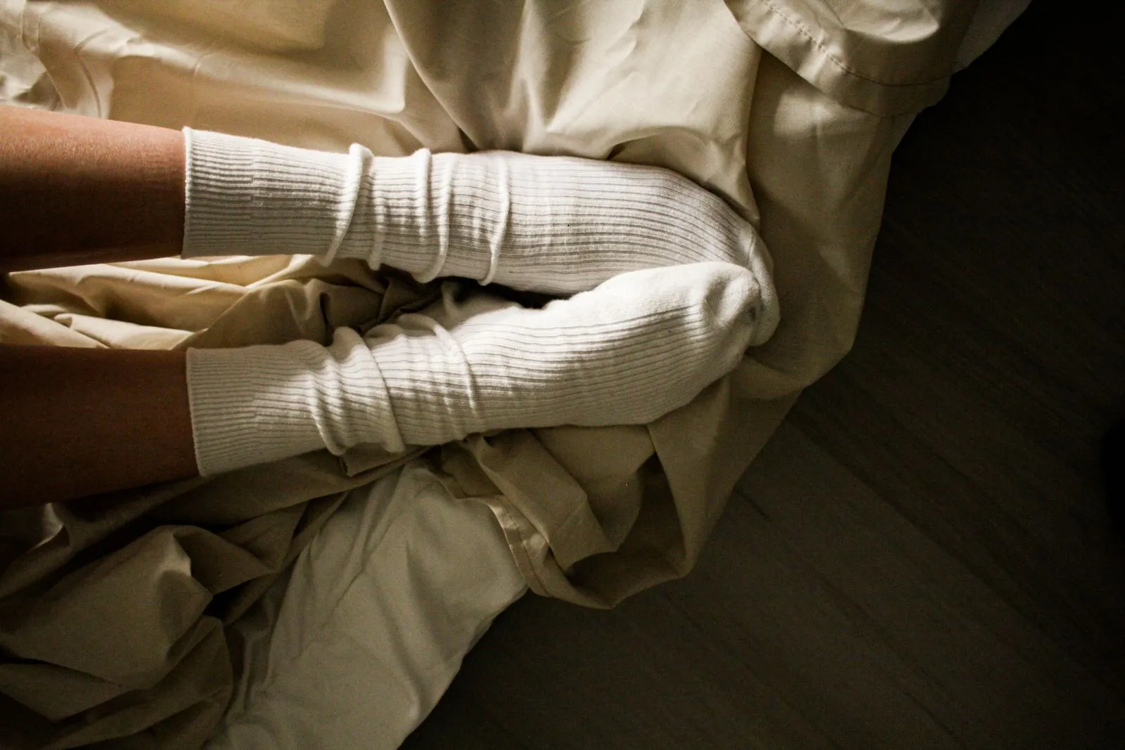 Legs in soft cream-colored socks resting on bedding in warm evening light