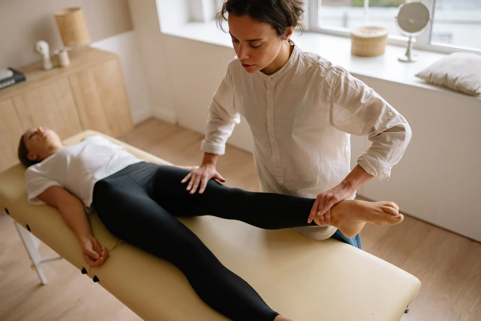 A physical therapist gently guiding a patient's leg during a calm rehabilitation session in a bright, home-like room