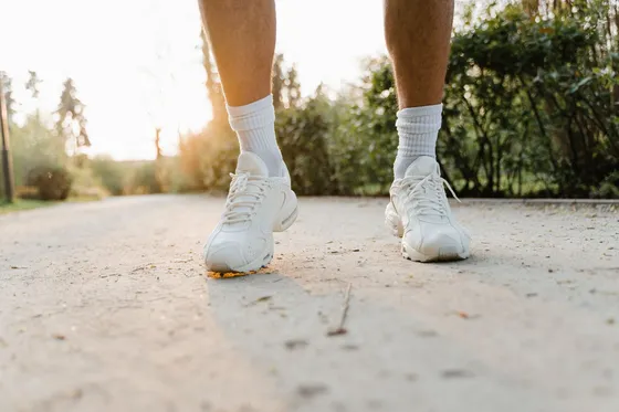 Feet in white sneakers and white socks standing on a sunlit path in warm evening light