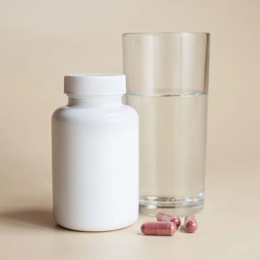 A plain supplement bottle beside a glass of water