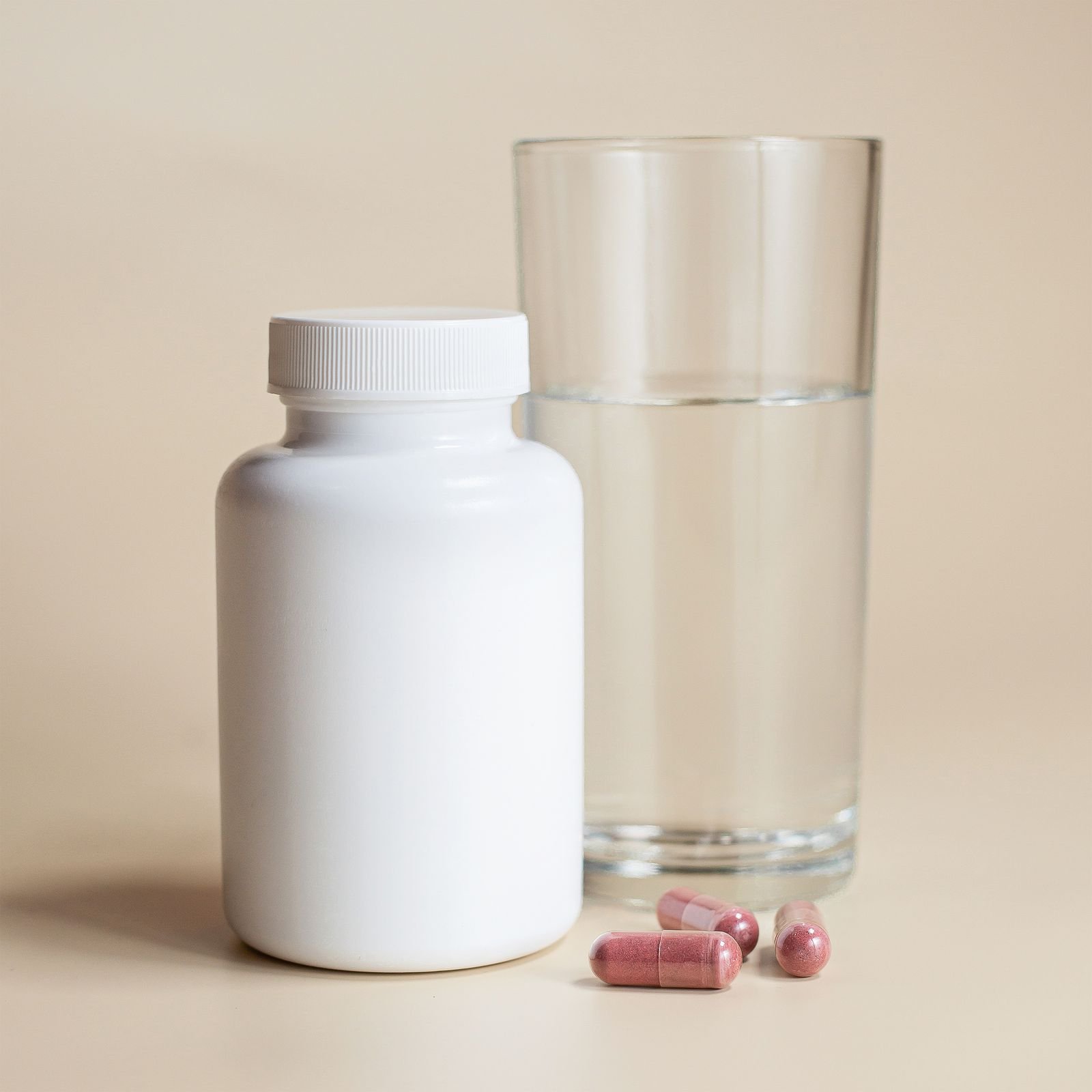 A plain supplement bottle beside a glass of water