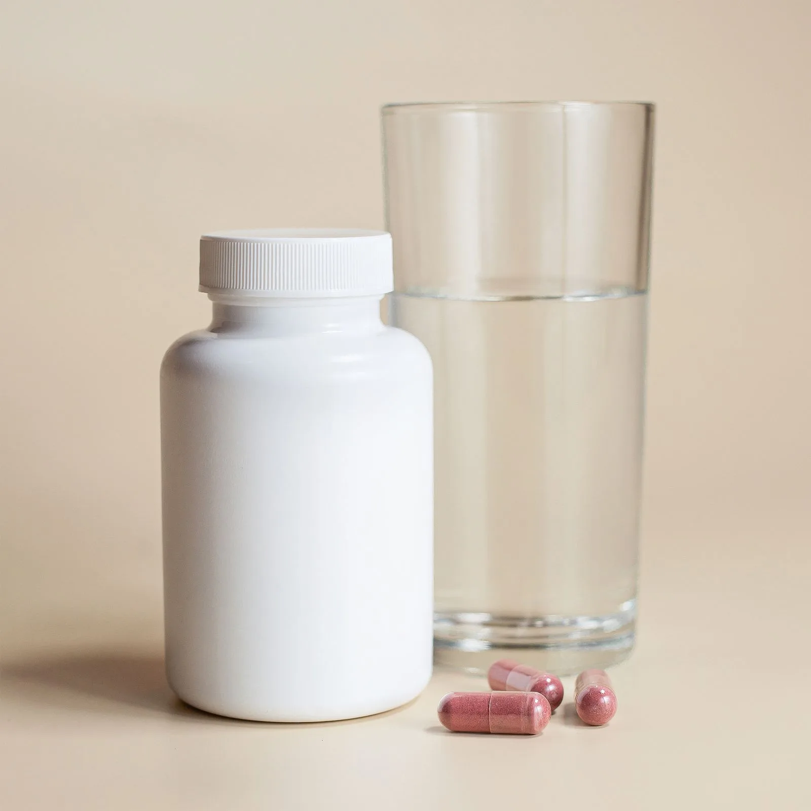 A plain white supplement bottle next to a glass of water and capsules, representing vitamin B12 testing and treatment
