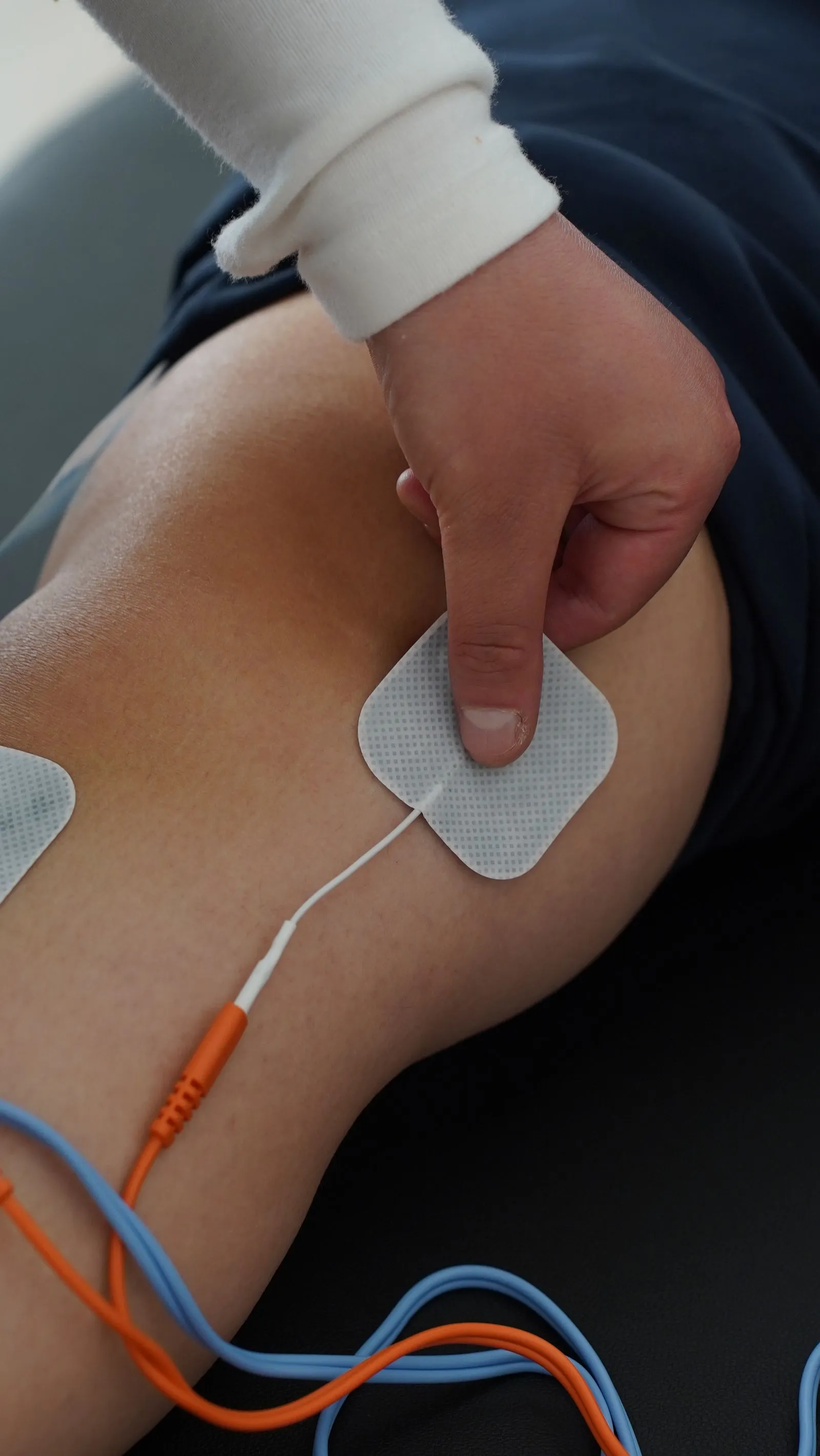 A hand carefully positioning a TENS electrode pad on the skin, with connecting wires visible