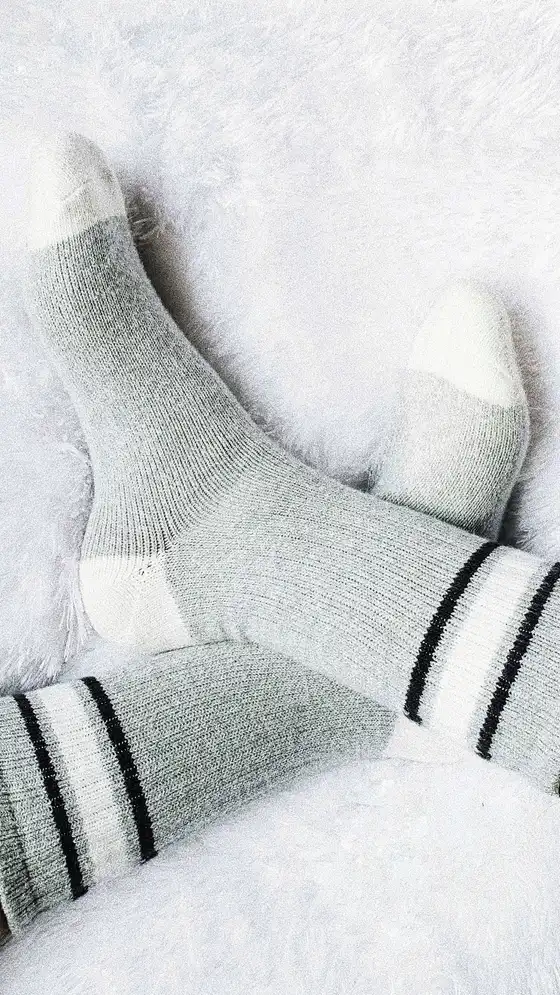 Feet in soft gray seamless wool socks resting on a white blanket, the kind of socks that suit neuropathy