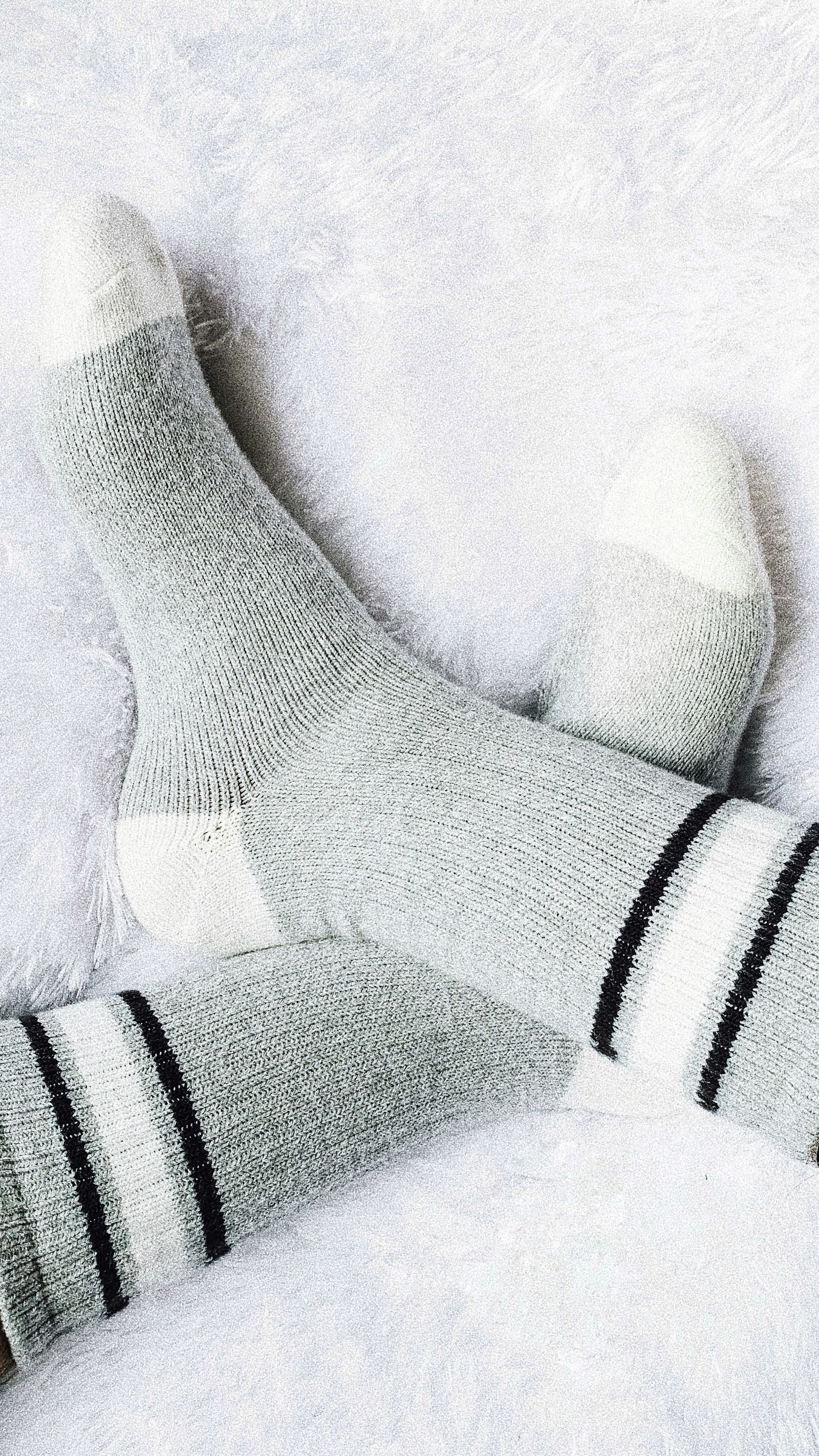 Feet in soft gray wool socks on a white blanket